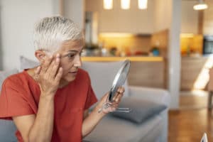 Photo of Attractive senior woman looking at her skin in the mirror. 