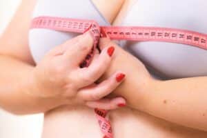 Woman measuring her large breasts, considering breast reduction