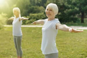 Two senior woman doing yoga in t-shirts, proudly showing off arms after brachioplasty.