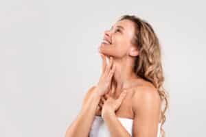 Smiling woman touching her chin and neck, showcasing a smooth jawline after Kybella treatment
