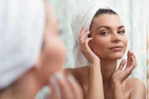 Woman fresh out of the shower and looking at her face in the mirror, considering cosmetic changes